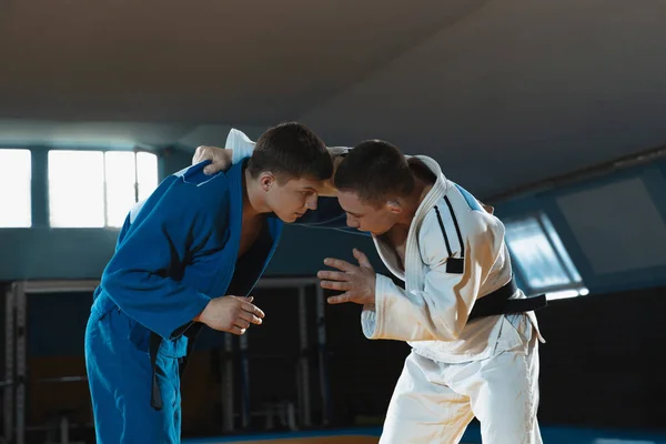Dos jóvenes luchadores de judo en kimono entrenando artes marciales en el gimnasio con expresión, en acción y movimiento —  Fotos de Stock