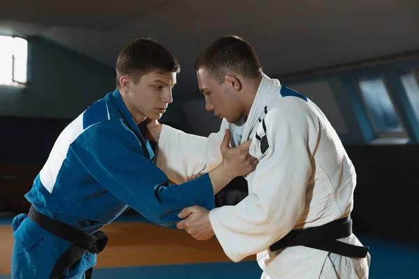 Dos jóvenes luchadores de judo en kimono entrenando artes marciales en el gimnasio con expresión, en acción y movimiento —  Fotos de Stock