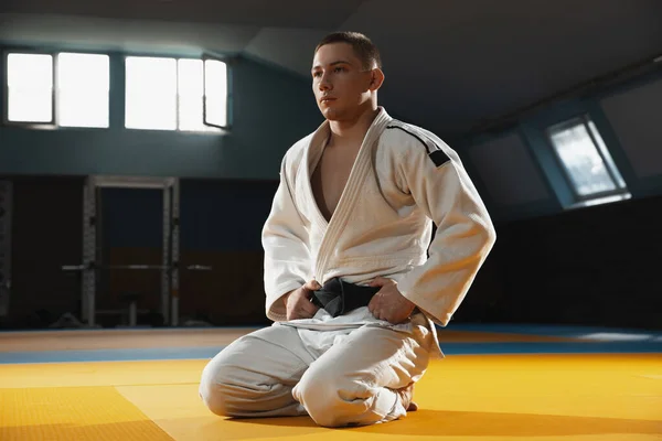 Fiatal judo harcos kimono pózol magabiztos az edzőteremben, erős és egészséges — Stock Fotó