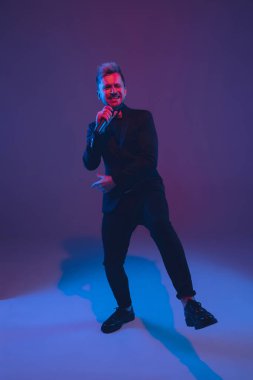 Beyaz tenli genç müzisyen, şarkı söyleyen, arka planda neon ışıkta dans eden