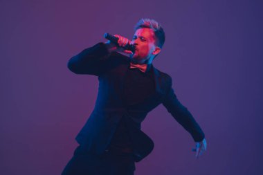 Beyaz tenli genç müzisyen, şarkı söyleyen, arka planda neon ışıkta dans eden