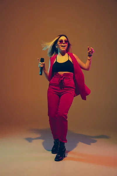 Jovem branco músico feminino, cantor cantando, dançando em luz de néon no fundo gradiente — Fotografia de Stock