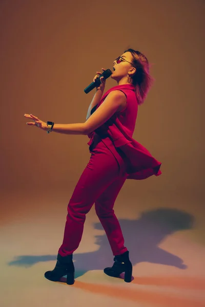 Jovem branco músico feminino, cantor cantando, dançando em luz de néon no fundo gradiente — Fotografia de Stock