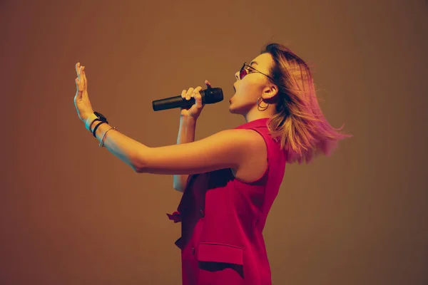 Joven músico femenino caucásico, intérprete cantando, bailando en luz de neón sobre fondo degradado —  Fotos de Stock