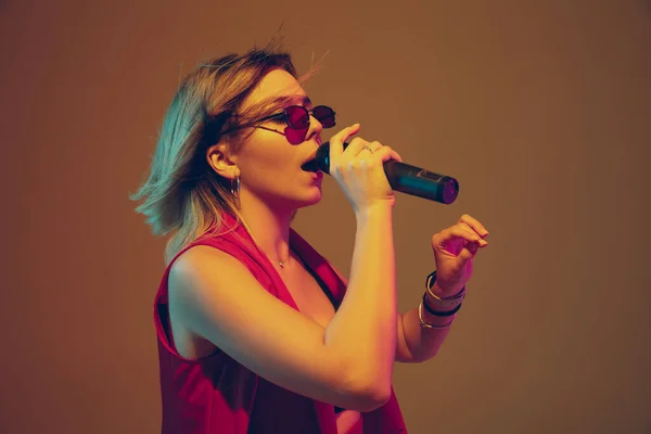 Jonge Kaukasische vrouwelijke muzikant, performer zingen, dansen in neon licht op gradiënt achtergrond — Stockfoto