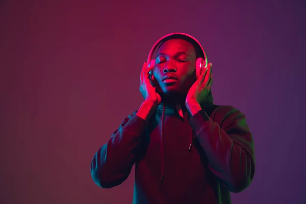 Retrato de hombre afroamericano con auriculares aislados sobre fondo de estudio degradado en luz de neón —  Fotos de Stock