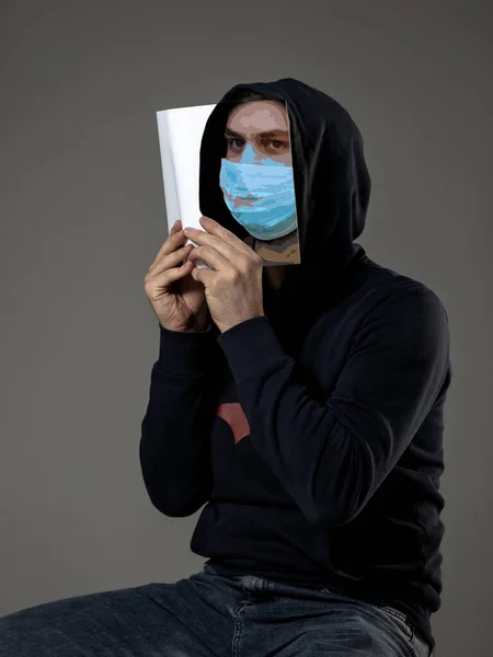 Bądź bezpieczny i czytaj, aby stać się kimś innym - człowiek zakrywający twarz książką w masce twarzy czytając na szarym tle — Zdjęcie stockowe