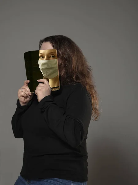 Wees veilig en lees om iemand anders te worden - vrouw die gezicht bedekt met boek in gezicht masker tijdens het lezen op grijze achtergrond — Stockfoto