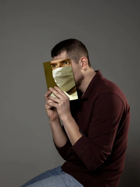 Будьте в безпеці і читайте, щоб стати кимось іншим - людина покриває обличчя книгою в масці для обличчя, читаючи на сірому фоні — стокове фото