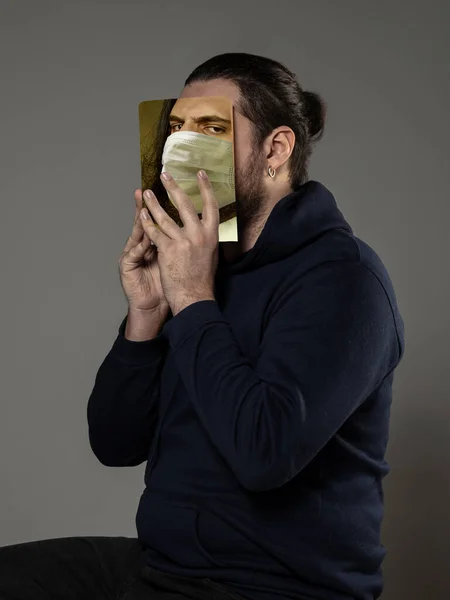 Auf Nummer sicher gehen und lesen, um jemand anderer zu werden - Mann verdeckt Gesicht mit Buch in Gesichtsmaske, während er auf grauem Hintergrund liest — Stockfoto