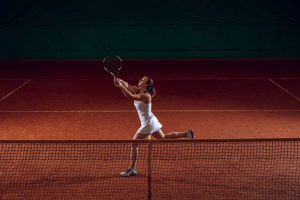 Joven deportista profesional caucásica jugando al tenis en el fondo de la cancha deportiva —  Fotos de Stock