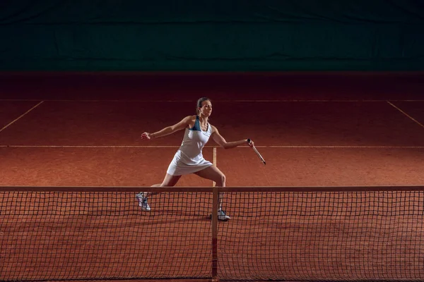 Молодая кавказская профессиональная спортсменка, играющая в теннис на спортивном фоне — стоковое фото