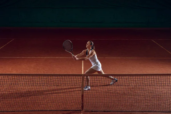 Νεαρή καυκάσια επαγγελματίας αθλήτρια που παίζει τένις στο γήπεδο του αθλητισμού φόντο — Φωτογραφία Αρχείου