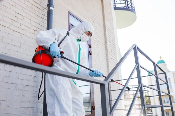 Coronavirus Pandemic. Disinfektor dalam pakaian pelindung dan masker menyemprotkan disinfektan di rumah atau kantor — Stok Foto