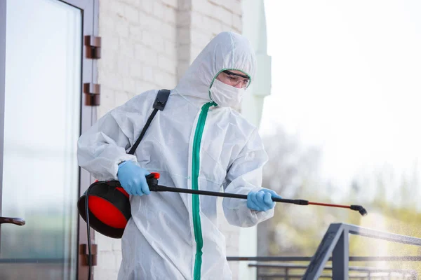 Coronavirus Pandemic. A disinfector in a protective suit and mask sprays disinfectants in the house or office