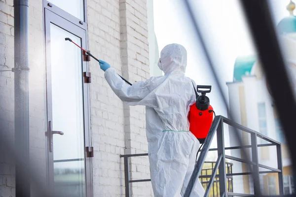 Coronavirus Pandemic. A disinfector in a protective suit and mask sprays disinfectants in the house or office — Stock Photo, Image