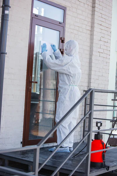Coronavírus Pandémico. Um desinfetor em um terno protetor e máscara pulveriza desinfetantes na casa ou escritório — Fotografia de Stock