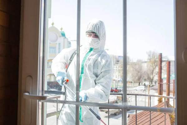 Coronavirus Pandemic. A disinfector in a protective suit and mask sprays disinfectants in the house or office — Stock Photo, Image