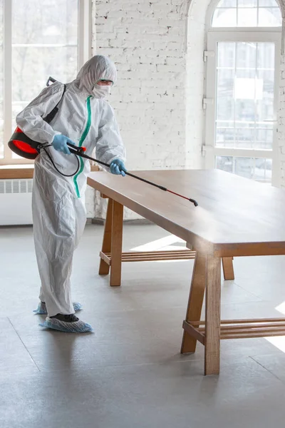 Pandemia por Coronavirus. Un desinfectante con traje protector y mascarilla pulveriza desinfectantes en la casa u oficina — Foto de Stock