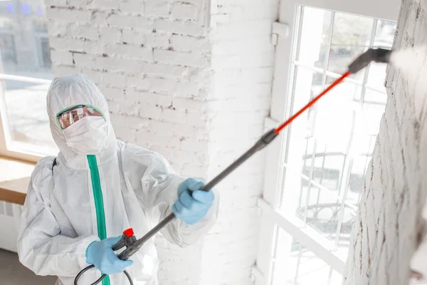 Pandemia di Coronavirus. Un disinfettante in tuta protettiva e maschera spruzza disinfettanti in casa o in ufficio — Foto Stock