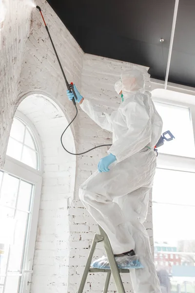 Pandemia por Coronavirus. Un desinfectante con traje protector y mascarilla pulveriza desinfectantes en la casa u oficina — Foto de Stock