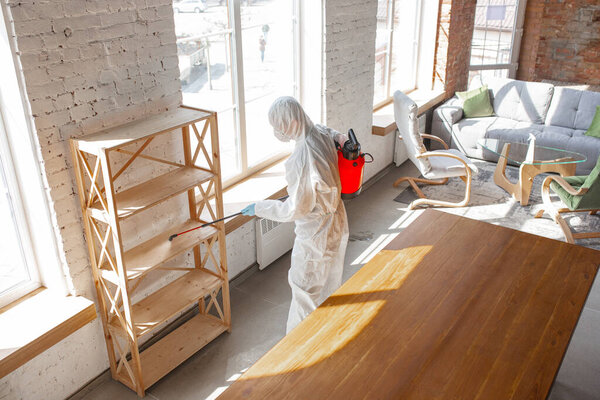 Coronavirus Pandemic. A disinfector in a protective suit and mask sprays disinfectants in the house or office