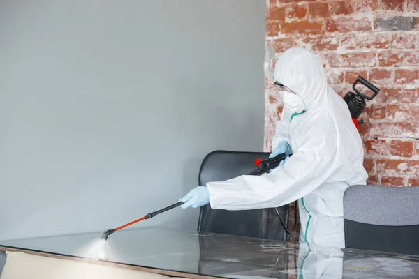 Coronavírus Pandémico. Um desinfetor em um terno protetor e máscara pulveriza desinfetantes na casa ou escritório — Fotografia de Stock