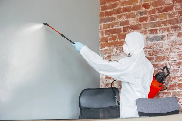 Coronavirus Pandemic. A disinfector in a protective suit and mask sprays disinfectants in the house or office — Stock Photo, Image