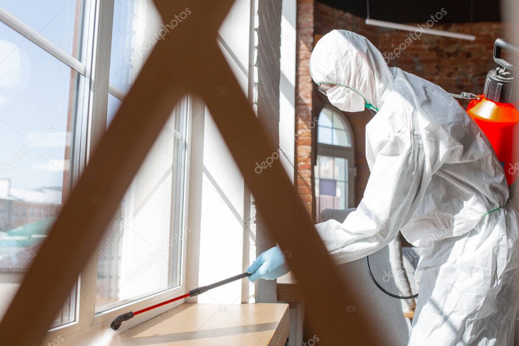 Coronavirus Pandemic. A disinfector in a protective suit and mask sprays disinfectants in the house or office