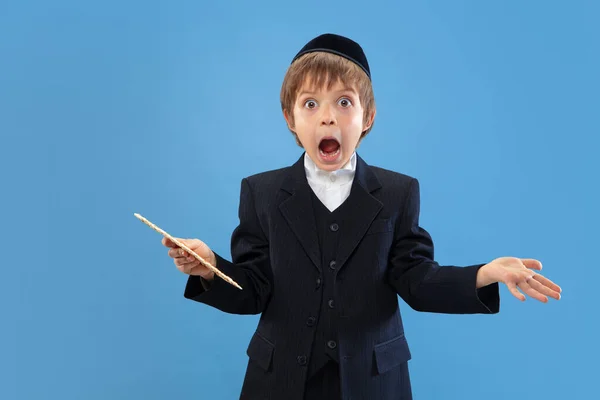 Портрет молодого ортодоксального єврейського хлопчика, ізольованого на синьому студійному фоні, що зустрічає Пасху — стокове фото