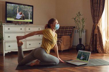 Sportif genç bir kadın karantinadayken yoga dersleri alıyor ve evde pratik yapıyor.