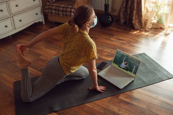 Sportieve jonge vrouw die online yoga lessen neemt en thuis oefent terwijl ze in quarantaine is — Stockfoto