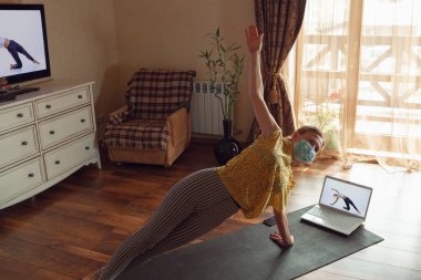 Sportif genç bir kadın karantinadayken yoga dersleri alıyor ve evde pratik yapıyor.