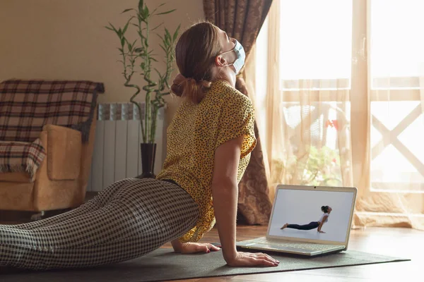 Sportliche junge Frau nimmt Yoga-Unterricht online und übt zu Hause unter Quarantäne — Stockfoto