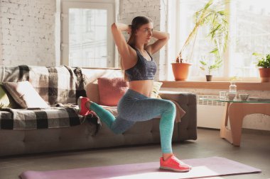Genç bir kadın karantinadayken evde online fitness, aerobik, sportif yaşam tarzı dersleri veriyor.