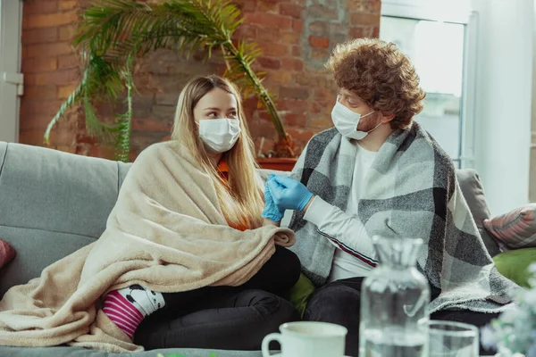 Mulher e homem, casal em máscaras protetoras e luvas isoladas em casa com sintomas de coronavírus — Fotografia de Stock