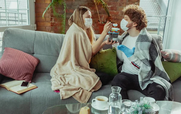 Mujer y hombre, pareja en máscaras protectoras y guantes aislados en casa con síntomas de coronavirus — Foto de Stock