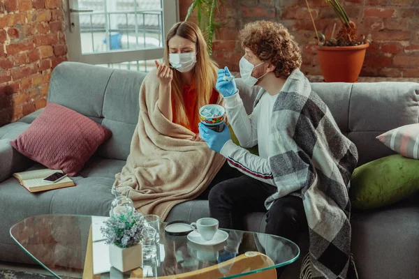 Mujer y hombre, pareja en máscaras protectoras y guantes aislados en casa con síntomas de coronavirus — Foto de Stock