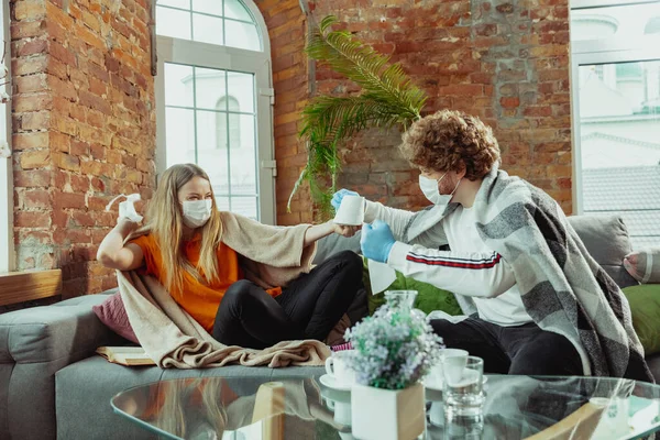 Женщина и мужчина, пара в защитных масках и перчатках изолированы дома с симптомами коронавируса — стоковое фото
