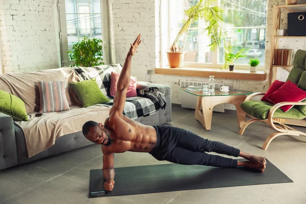 Giovane uomo afro-americano che insegna a casa corsi online di fitness, aerobica, stile di vita sportivo pur essendo in quarantena — Foto Stock