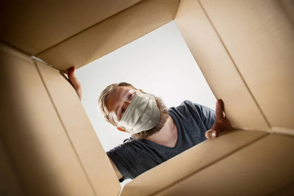 Young man opening the huge postal package wearing protective face mask, contactless delivery — Stock Photo, Image