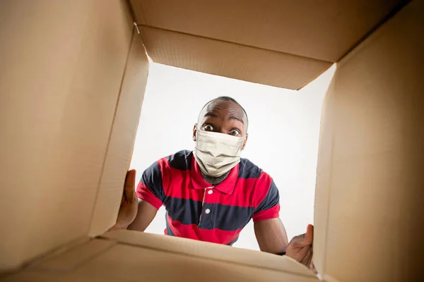 Young man opening the huge postal package wearing protective face mask, contactless delivery — Stock Photo, Image