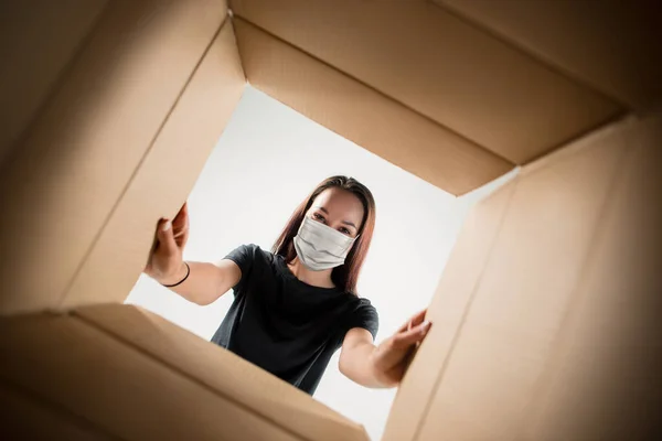 Genç bir kadın koruyucu maske takarak büyük bir posta paketini açıyor. — Stok fotoğraf