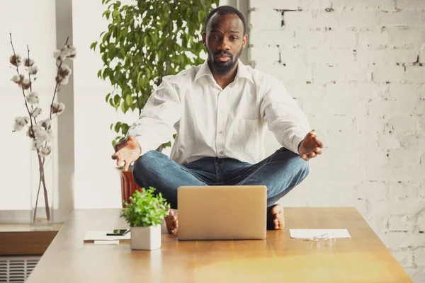 Joven hombre afroamericano haciendo yoga en casa mientras está en cuarentena y trabajando por cuenta propia — Foto de Stock