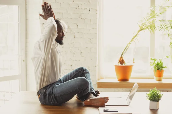 Ung afrikansk-amerikansk man som yogar hemma medan han är karantän och frilansar. — Stockfoto