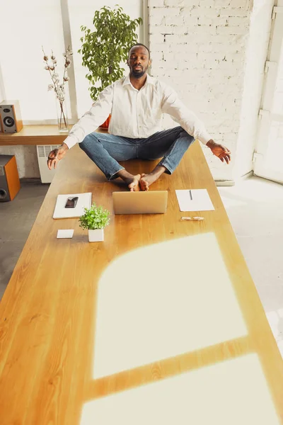 Joven hombre afroamericano haciendo yoga en casa mientras está en cuarentena y trabajando por cuenta propia — Foto de Stock