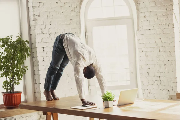 Joven hombre afroamericano haciendo yoga en casa mientras está en cuarentena y trabajando por cuenta propia — Foto de Stock