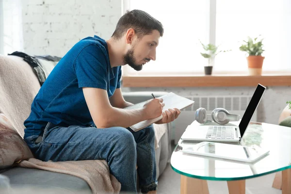 Hombre joven enfocado que estudia en casa durante cursos en línea o información gratuita por sí mismo — Foto de Stock