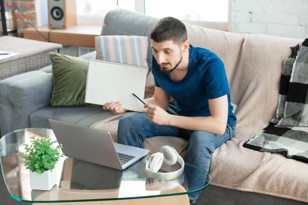 Hombre joven enfocado que estudia en casa durante cursos en línea o información gratuita por sí mismo — Foto de Stock