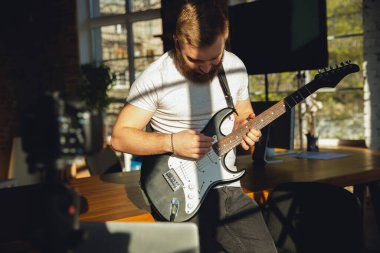 Beyaz müzisyen evdeki online konser sırasında gitar çalıyor izole ve karantinaya alınmış, etkileyici bir doğaçlama.